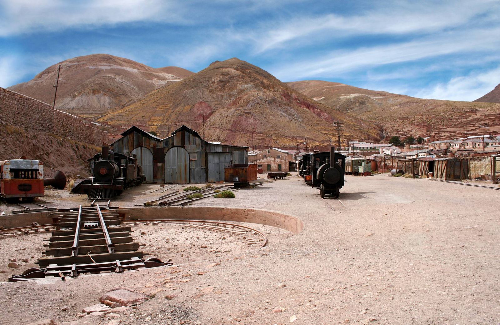 Antiguo depósito ferroviario con locomotoras y cerros rojizos