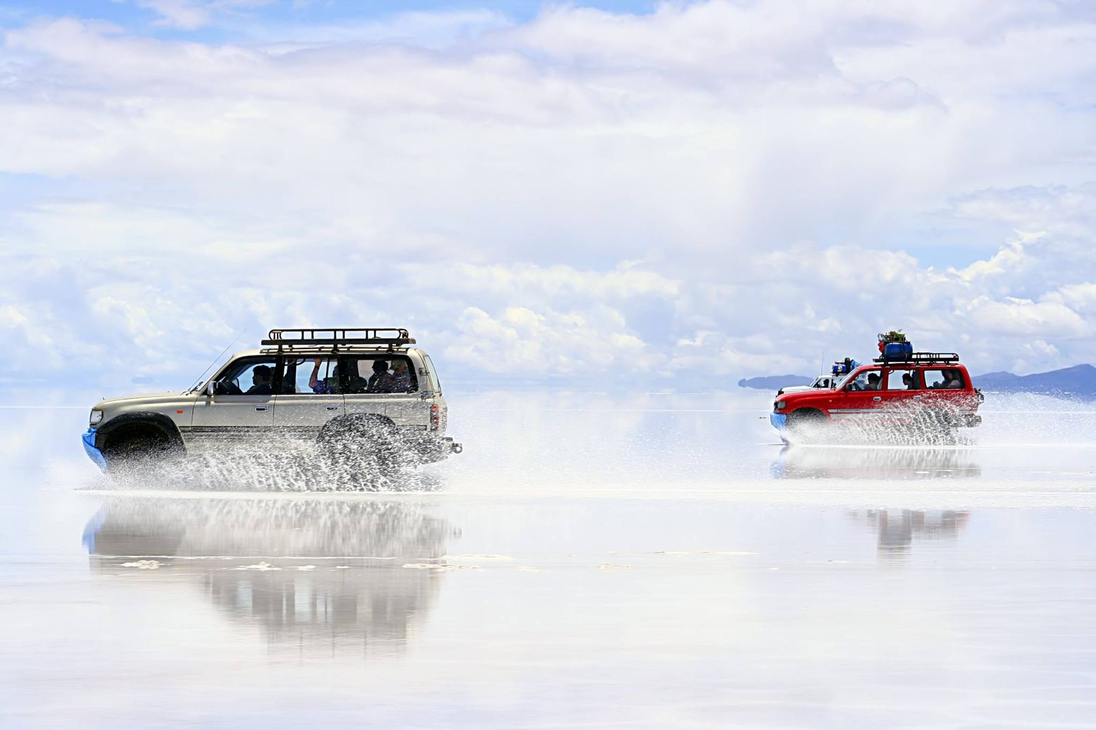 Deux 4x4 roulant sur le salar recouvert d’eau en soulevant des éclaboussures, avec le ciel reflété