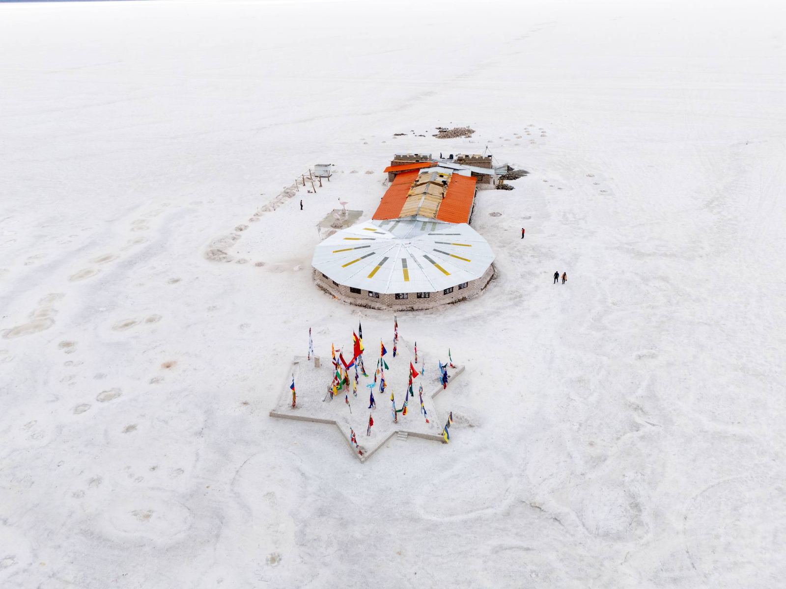 Vue aérienne d’un bâtiment rond au toit orange et d’une place en forme d’étoile ornée de drapeaux, sur le salar blanc