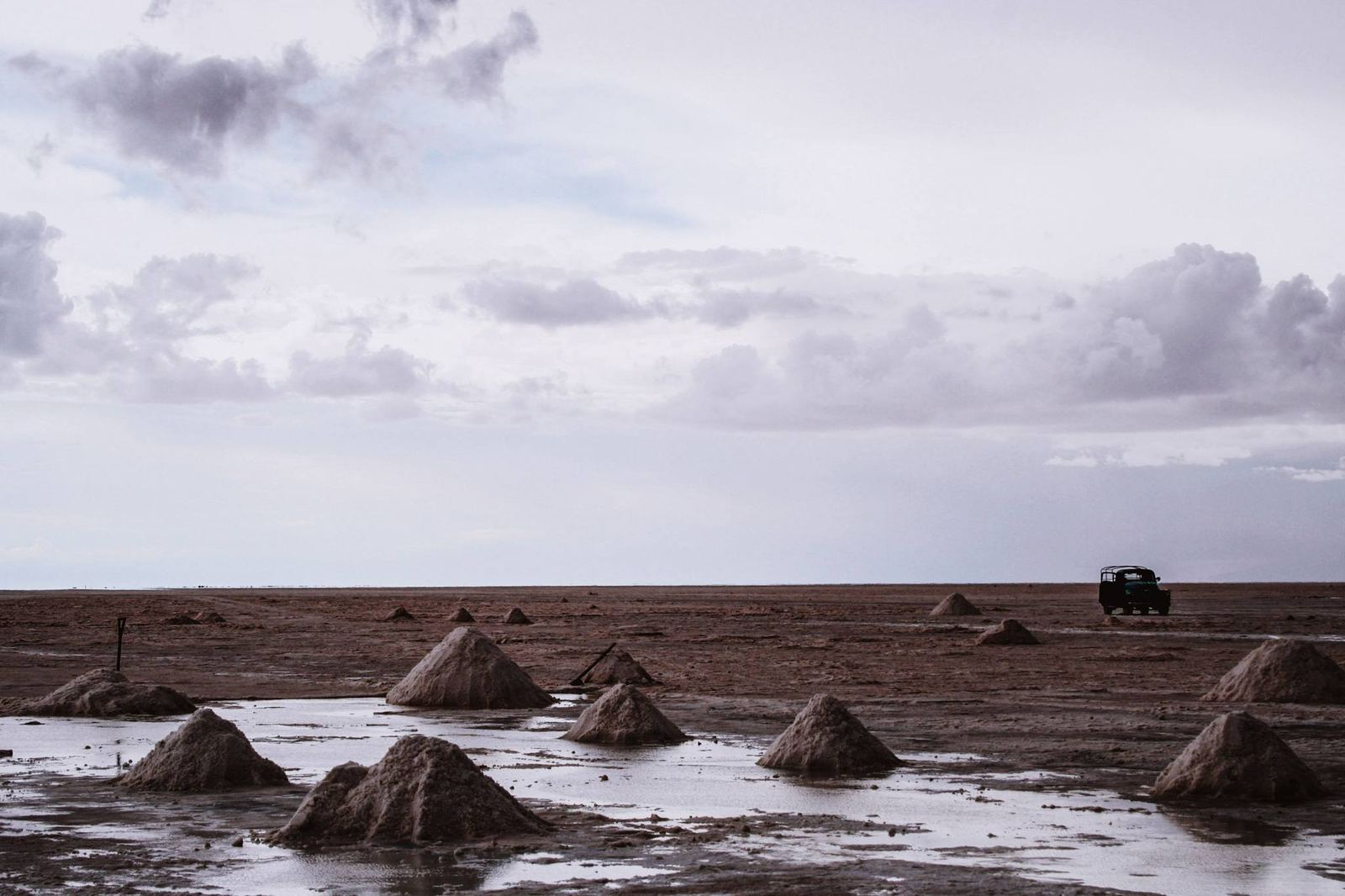 Montones de sal alineados sobre el salar, con charcos y un 4x4 a lo lejos